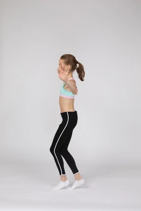 Vista lateral de una jovencita en ropa deportiva de equilibrio de puntillas mientras levanta las manos