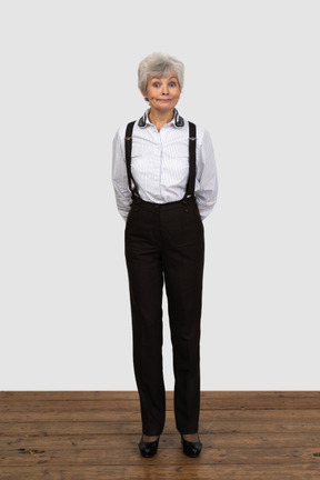 Front view of an old displeased female in office clothes grimacing with her hands behind back