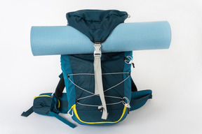 Blauer touristischer rucksack mit einer yogamatte auf einem weißen hintergrund