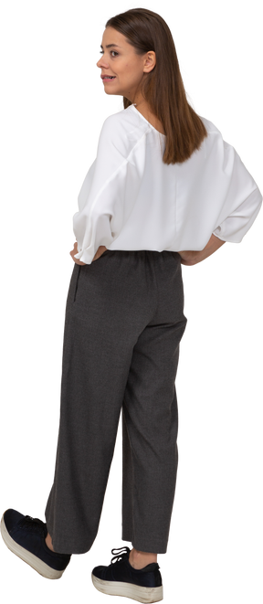Vista posteriore di tre quarti di una giovane donna arrogante in abiti da ufficio che mette le mani sui fianchi