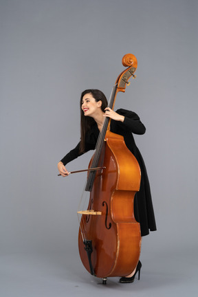 Vista frontale di una giovane donna sorridente in abito nero che suona il contrabbasso con un arco