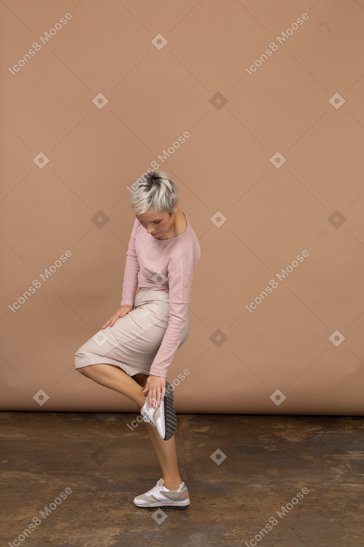 Side view of a woman in casual clothes standing on one leg and touching her shoe