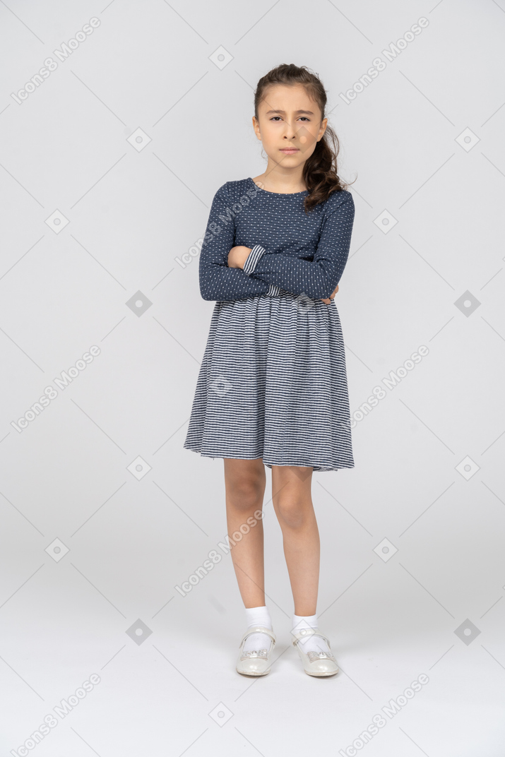 Vista frontal de una niña entrecerrando los ojos sospechosamente con las manos cruzadas