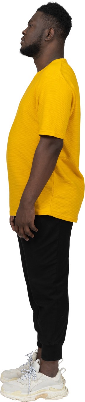 Side view of a young dark-skinned man in yellow t-shirt standing still