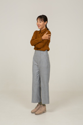 Vista di tre quarti di una giovane donna asiatica in calzoni e camicetta che si abbraccia