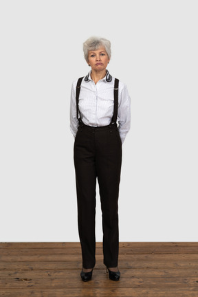 Vista frontal de una vieja mujer disgustada en ropa de oficina con las manos detrás de la espalda