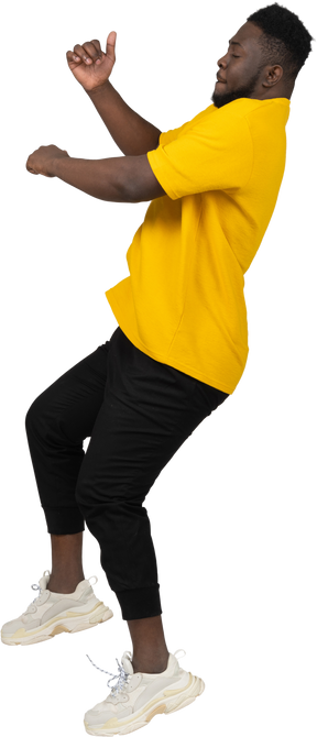 Vista lateral de un joven de piel oscura con camiseta amarilla saltando hacia atrás