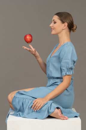 Вид сбоку на веселую молодую женщину, бросающую яблоко