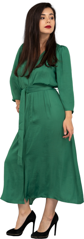 Dreiviertelansicht einer stolzen jungen dame im grünen kleid, die hand auf hüfte legt