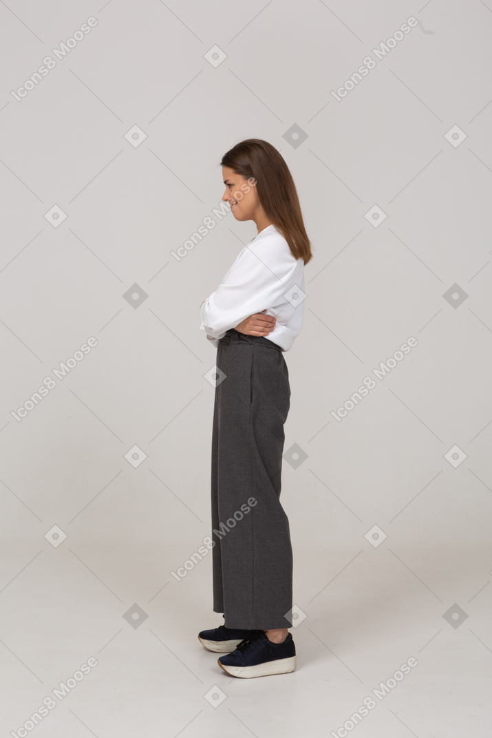 Vista laterale di una giovane donna furba in abiti da ufficio che incrociano le braccia
