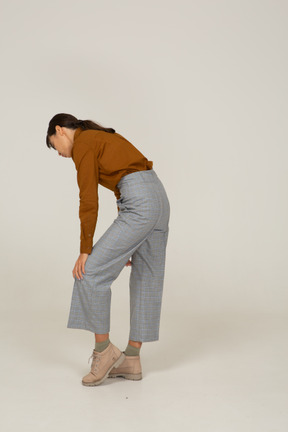 Vista posterior de tres cuartos de una joven mujer asiática en calzones y blusa inclinada hacia adelante