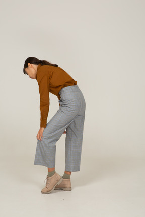 Three-quarter back view of a young asian female in breeches and blouse leaning forward