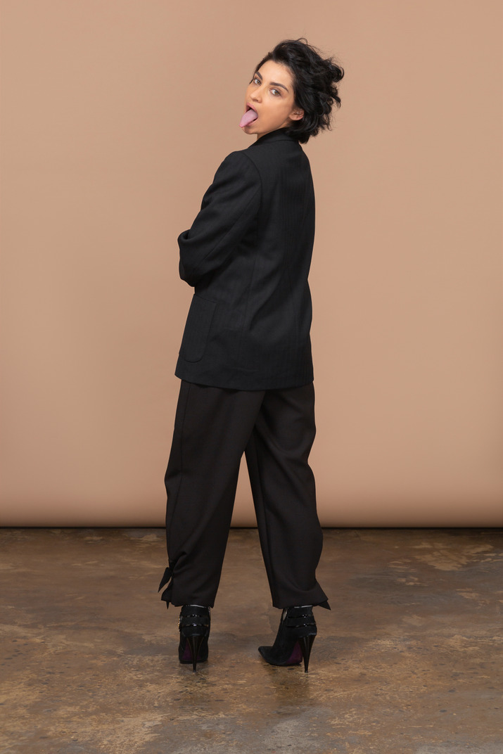 Back view of a businesswoman wearing black suit and showing tongue while looking at camera