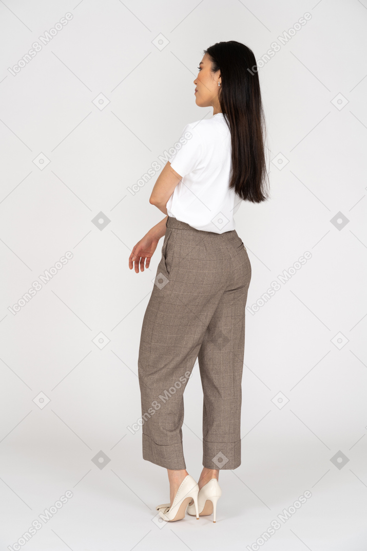 Three-quarter back view of a thoughtful young woman in breeches putting hand on stomach