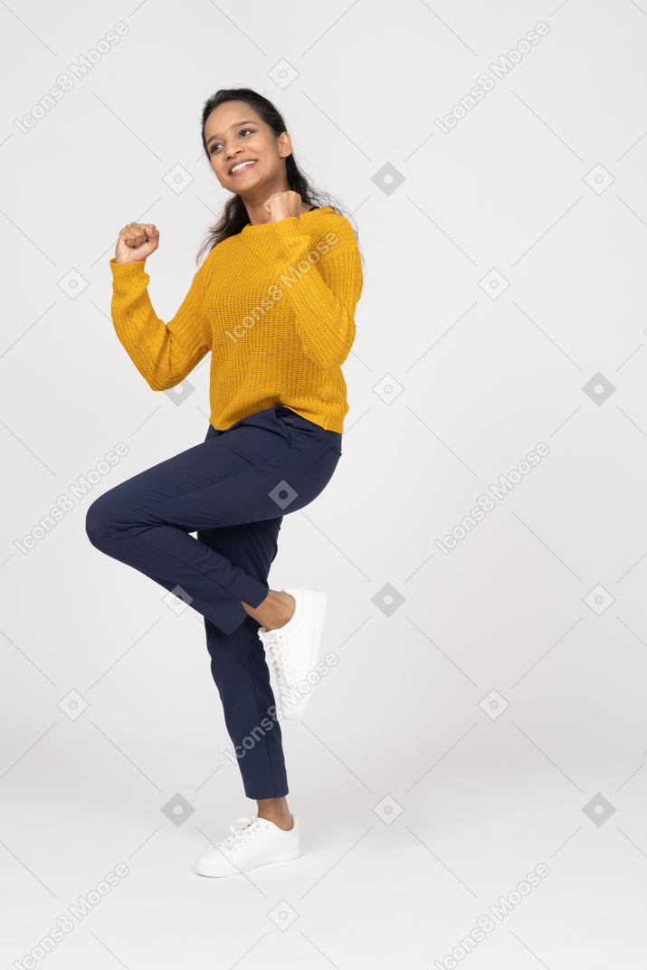 一个穿着休闲服、单腿摆姿势的快乐女孩的前视图