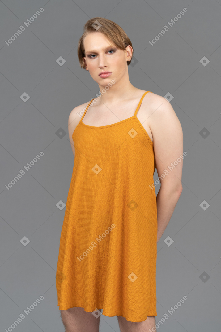 一个身穿橙色连衣裙、双手背在身后的性别酷儿肖像