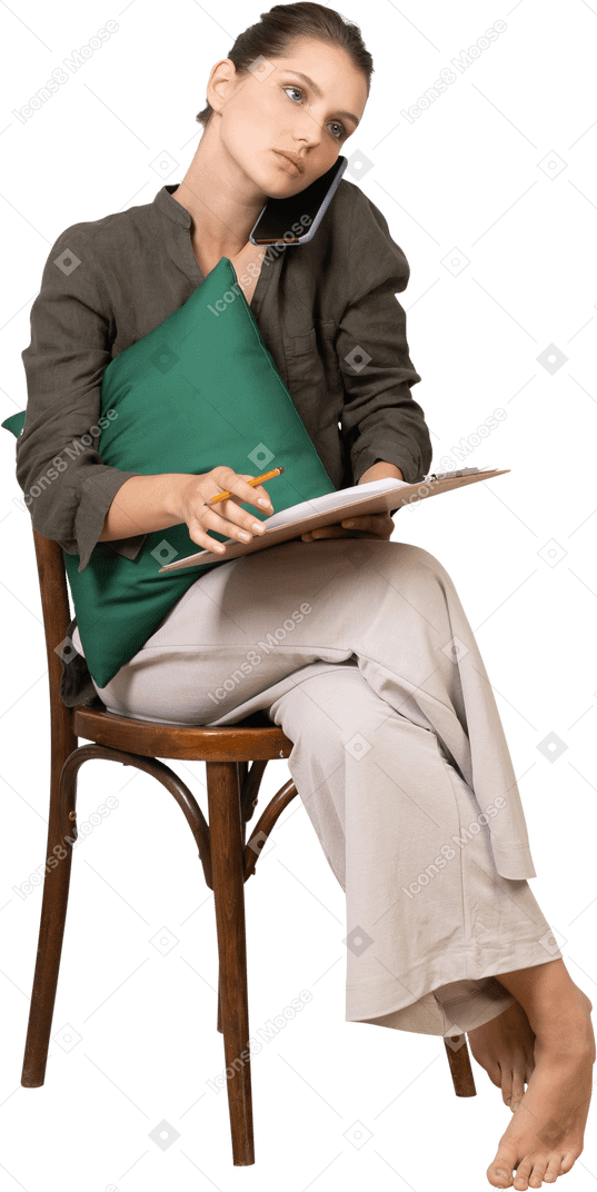 Vista frontale di una giovane donna seduta su una sedia con un tablet e che fa una telefonata