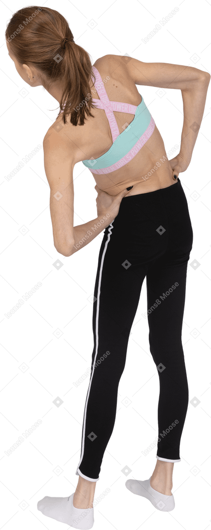 Vista posterior de tres cuartos de una jovencita en ropa deportiva poniendo las manos en las caderas mientras se inclina hacia la izquierda