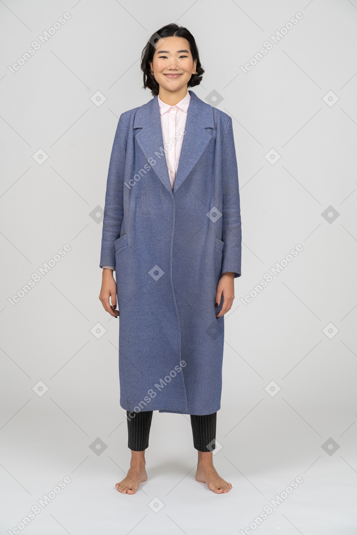 Улыбающаяся женщина в синем пальто, стоящая с руками по бокам
