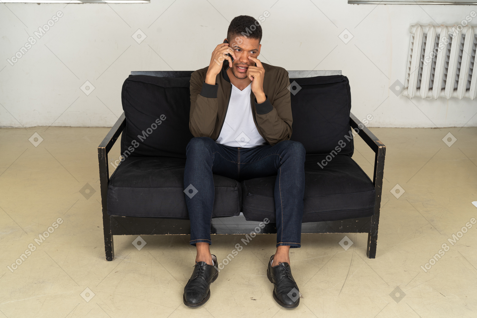 Vista frontale di un giovane perplesso seduto su un divano
