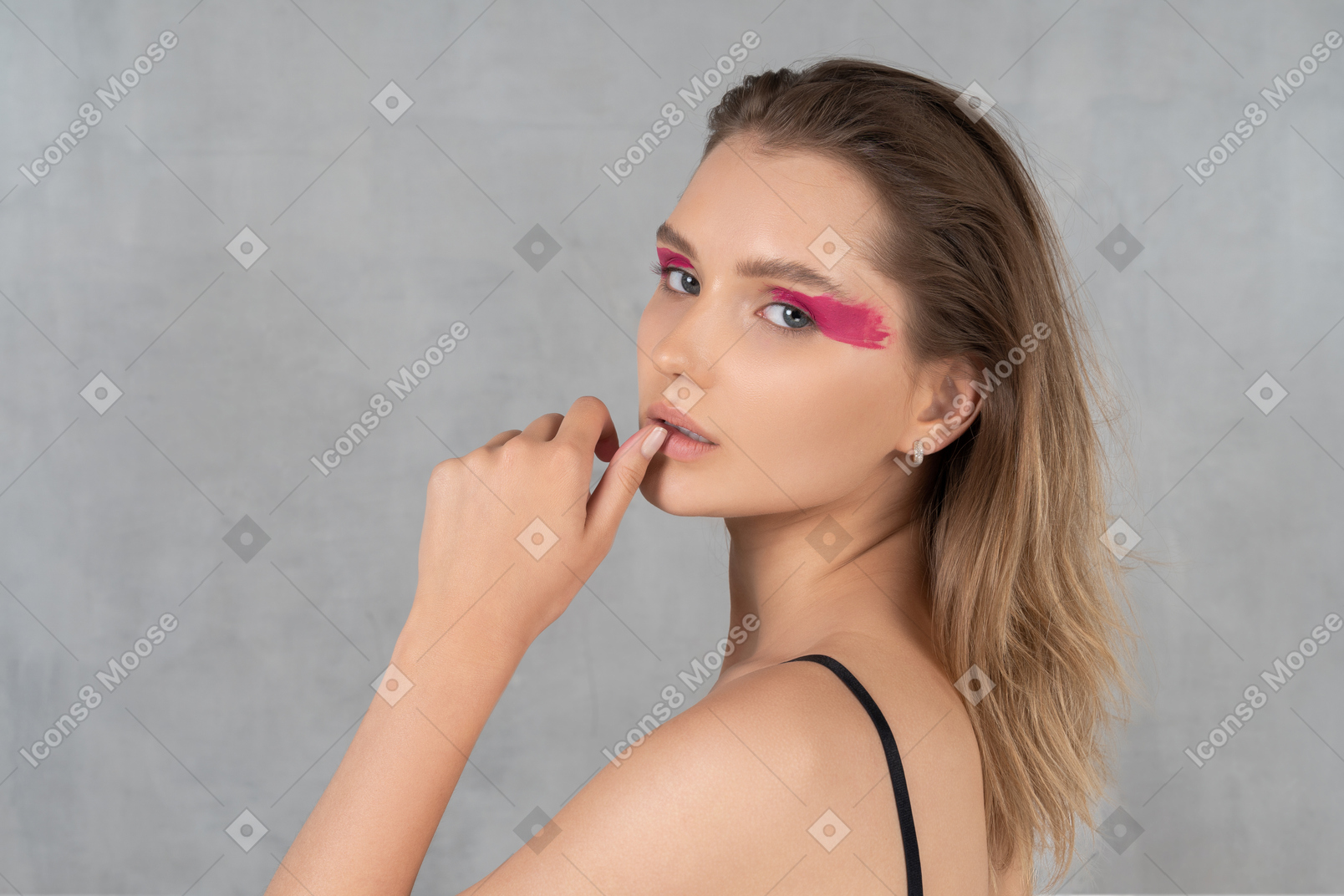 Attractive young woman with bold eye make-up holding thumb to lips
