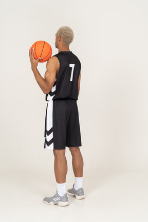 Vista traseira a três quartos de um jovem jogador de basquete segurando uma bola