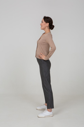 Vista laterale di una giovane donna sorridente in pullover e pantaloni mettendo le mani sui fianchi