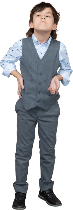 Vista frontal de un chico lindo con traje gris posando con la mano en la cadera y mirando hacia arriba