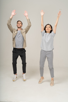 Young woman and man standing on toes with hands up