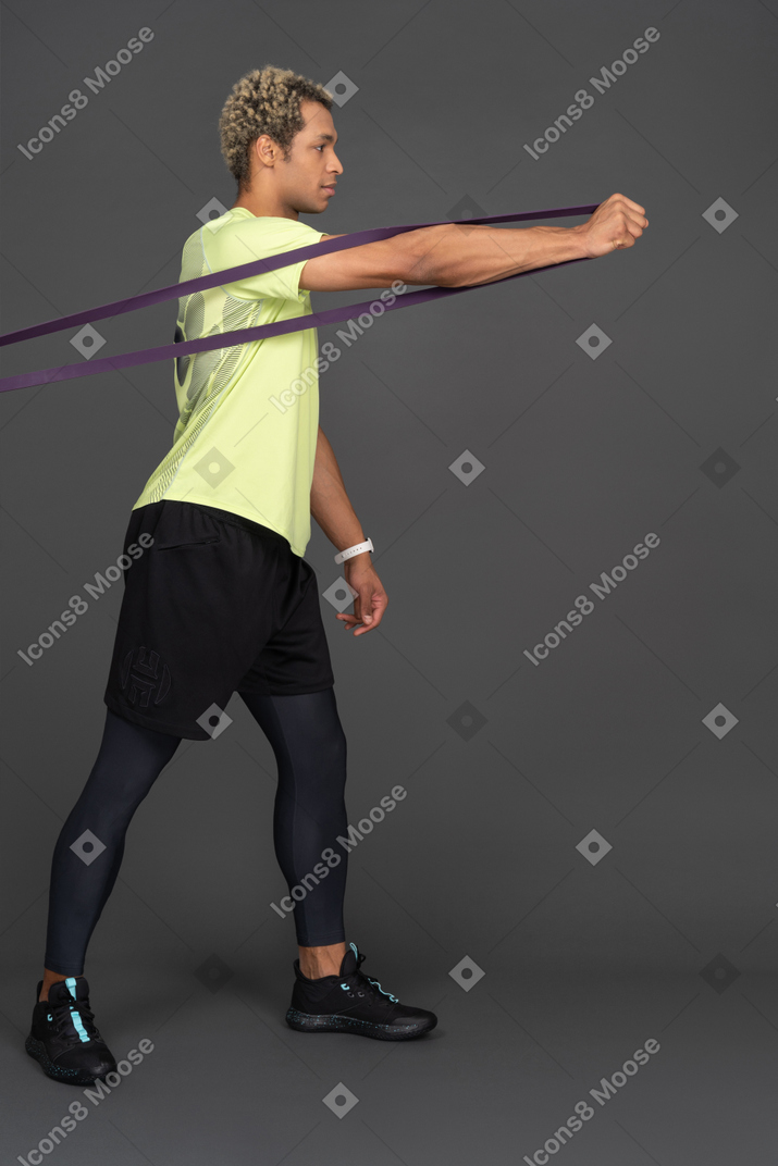 Side view of a dark-skinned young man pulling forward an elastic rubber