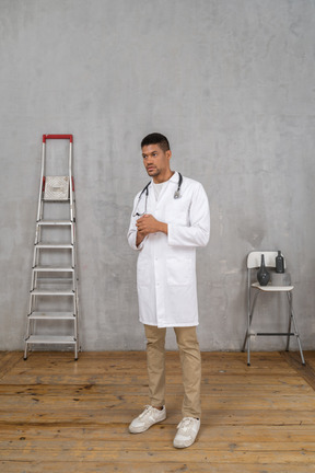 Vista de tres cuartos de un joven médico de pie en una habitación con escalera y silla tomados de la mano juntos