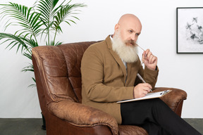 A bald man sitting in a chair with a pen in his mouth