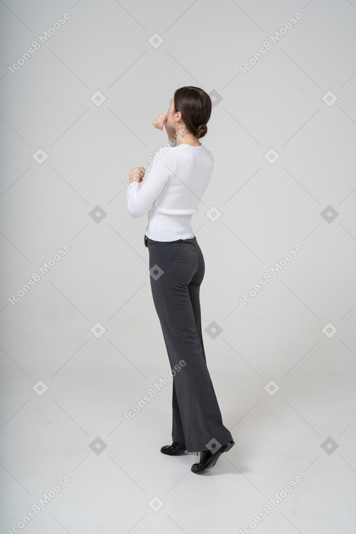 Молодая женщина в черных брюках и белой блузке позирует в профиль