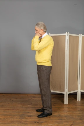 Side view of an old man clenching fists and touching face