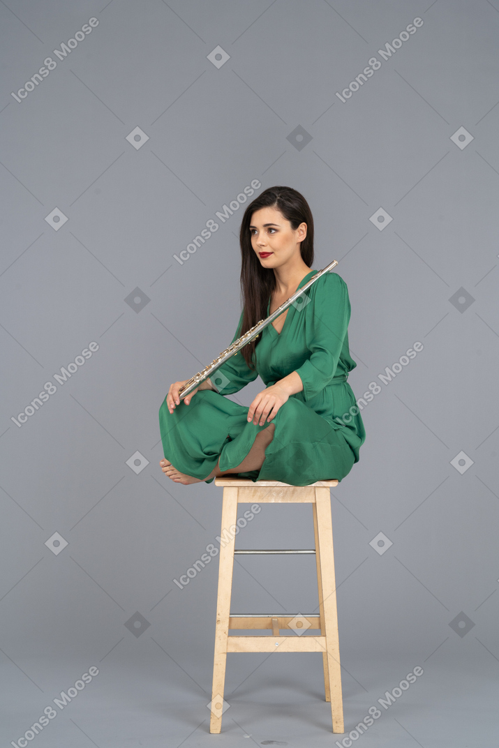 Toute la longueur d'une jeune femme tenant la clarinette assise, les jambes croisées sur une chaise en bois