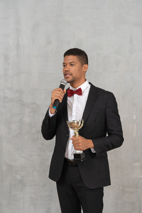 Man speaking into microphone and holding trophy