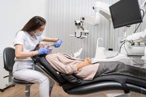 Женщина-стоматолог в полный рост осматривает своего пациента в больничном кабинете