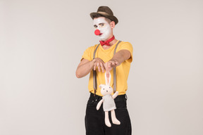 Male clown looking with a little bit of disgust at toy rabbit he's holding