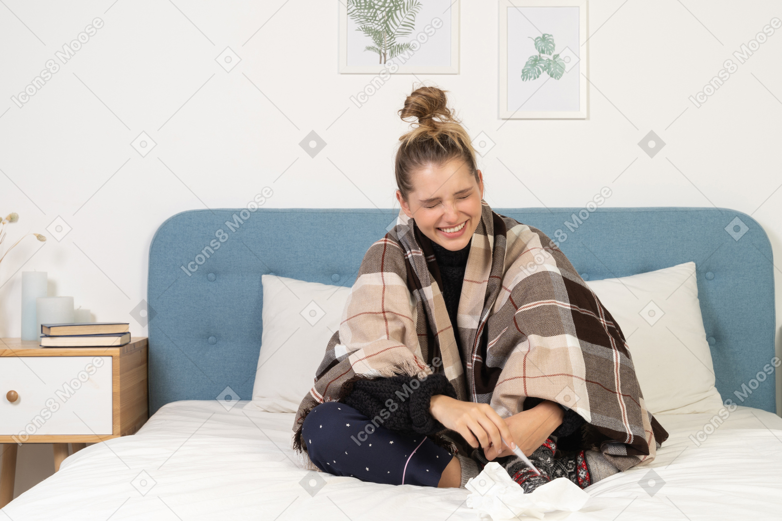 Front view of a laughing ill young lady in pajamas wrapped in checked blanket with thermometer