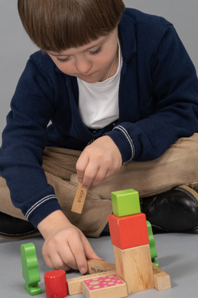 Fokussierter kleiner junge, der mit holzwürfeln spielt