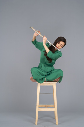Comprimento total de uma jovem tocando clarinete sentada com as pernas cruzadas em uma cadeira de madeira