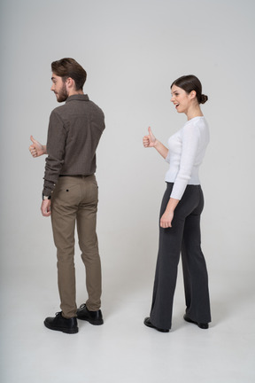 Three-quarter back view of a cheerful young couple in office clothing showing thumb up
