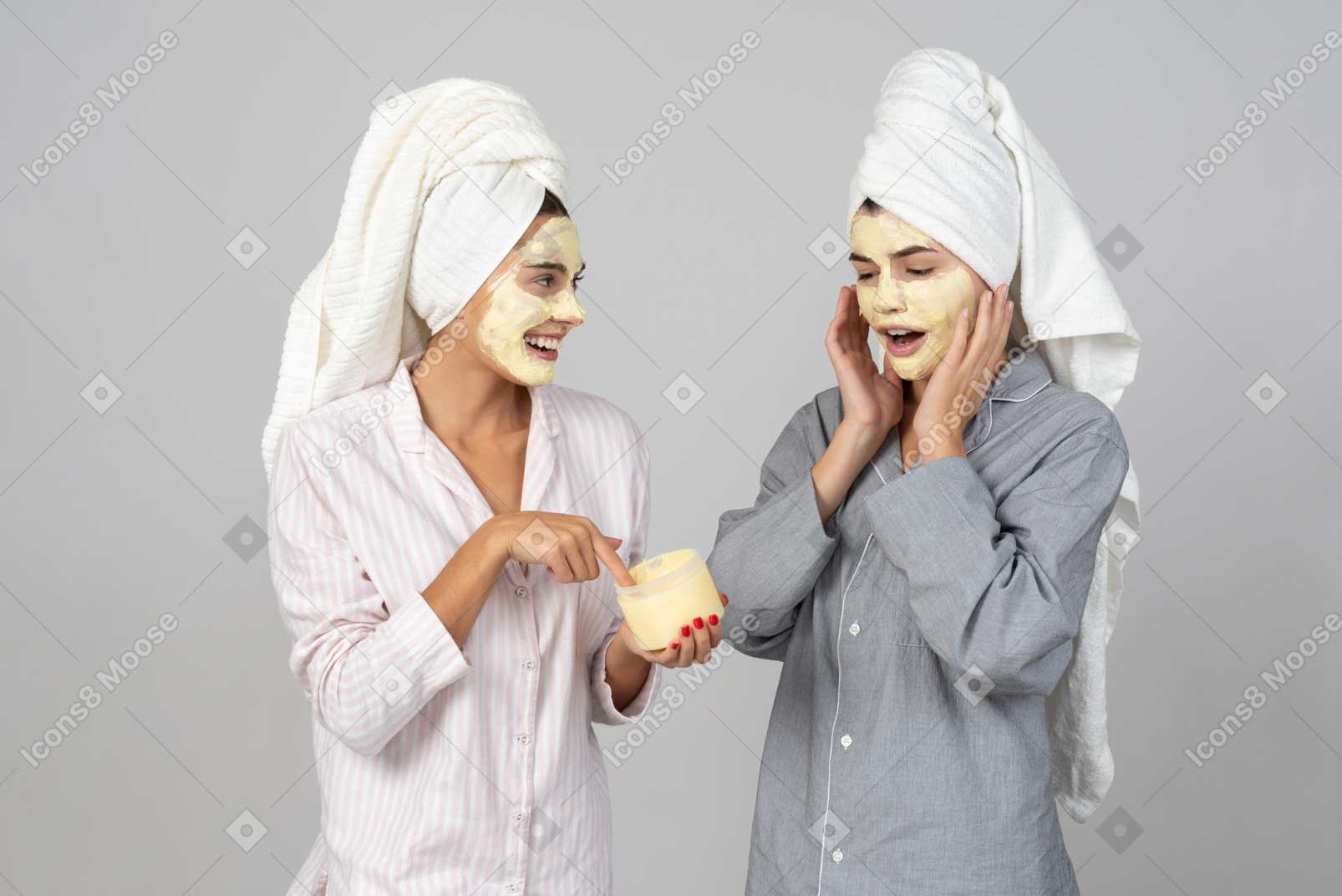 Две молодые девушки с волосами, завернутыми в полотенца, наносят крем-маски на лицо