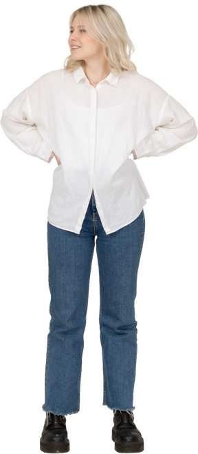 Vista frontale di una donna bionda in abiti casual, mettendo le mani sui fianchi e guardando da parte mentre sorride