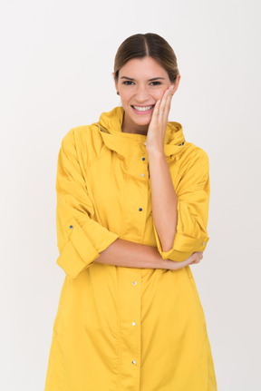 Young woman in yellow raincoat smiling and touching her cheek with an arm