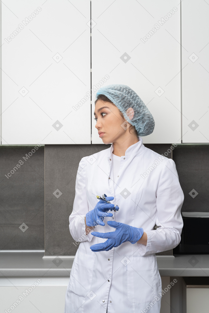Front view of a nurse in a medical hat holding a syringe and looking aside