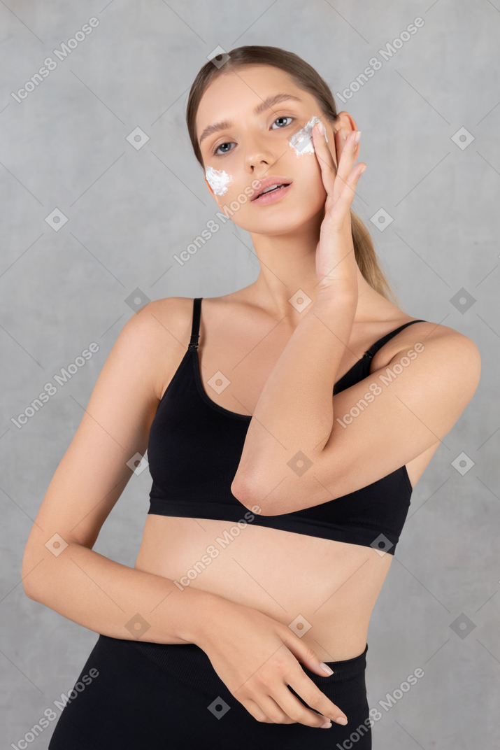 Young beautiful woman applying moisturizer on her cheeks
