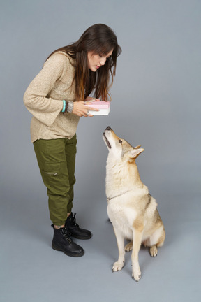 De cuerpo entero de una hembra joven inclinada sobre su perro y sosteniendo un regalo