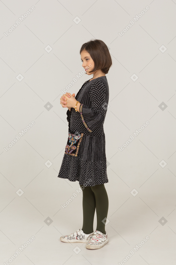 Side view of a sly little girl in dress holding hands together