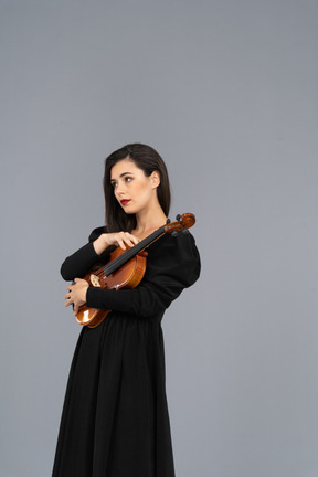 Vue de trois quarts d'une jeune femme en robe noire tenant le violon